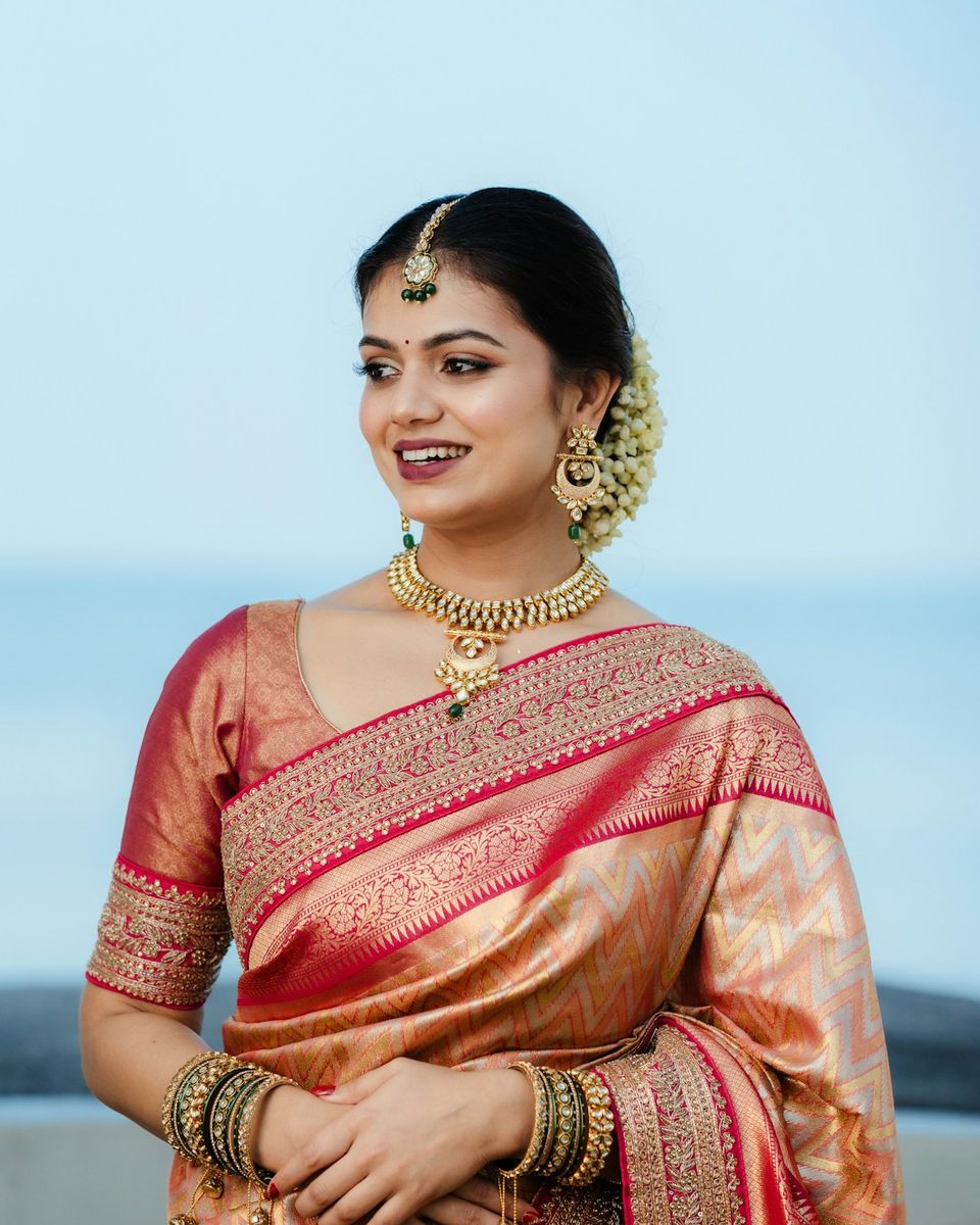 A smiling bride in a red and gold silk saree, with soft, natural-looking makeup and jasmine in her hair.