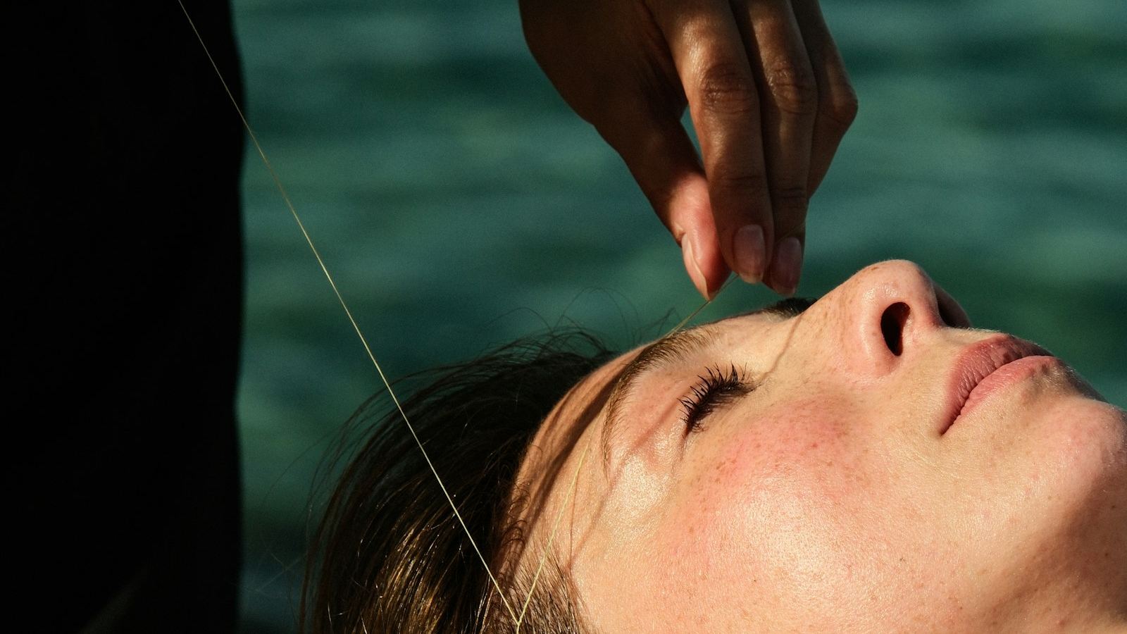 A therapist threading a woman’s eyebrow, the cotton thread held taut between her fingers.