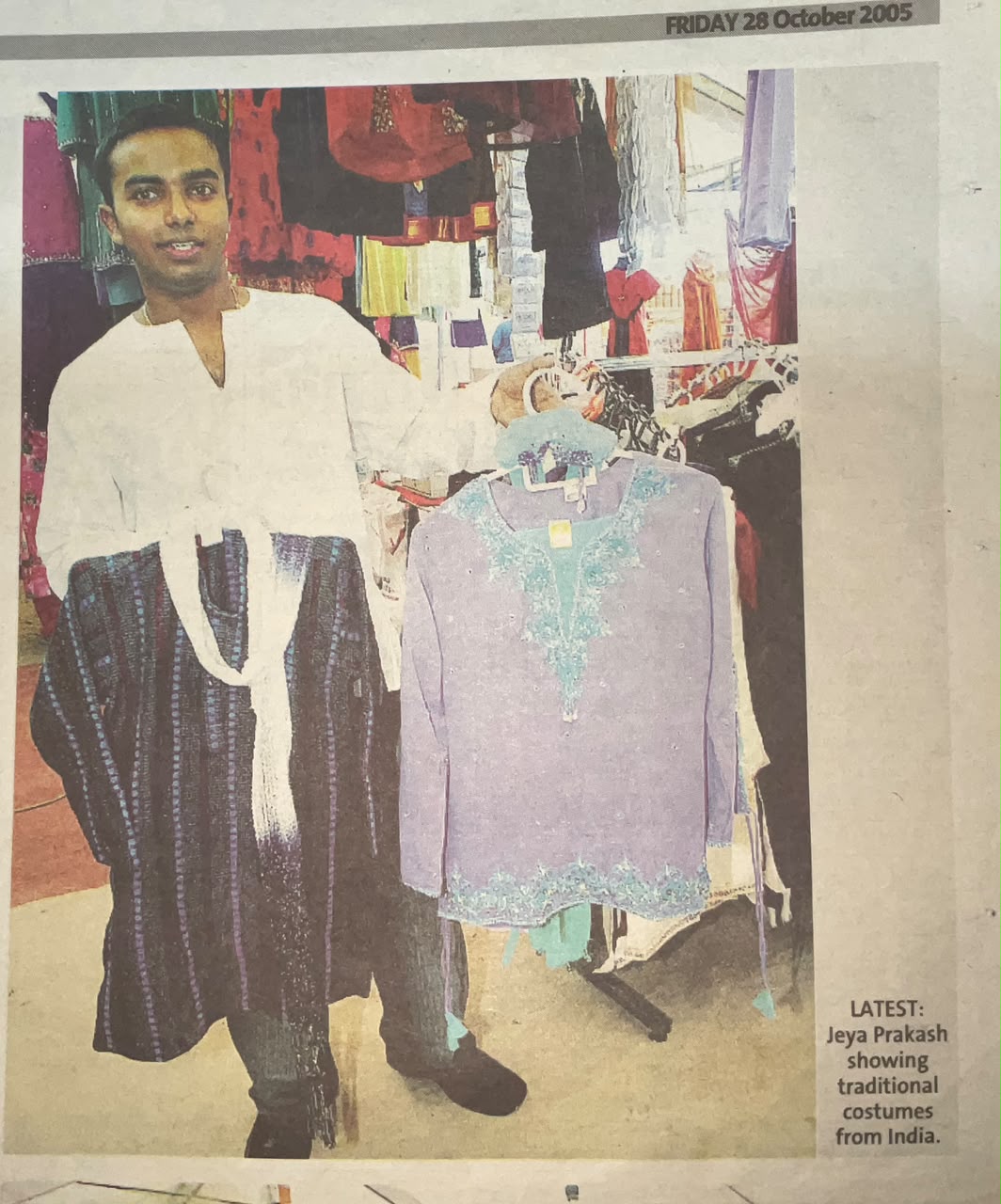 Newspaper photograph of Mr Jeya Prakash holding up two traditional Indian shirts in front of racks of clothing.